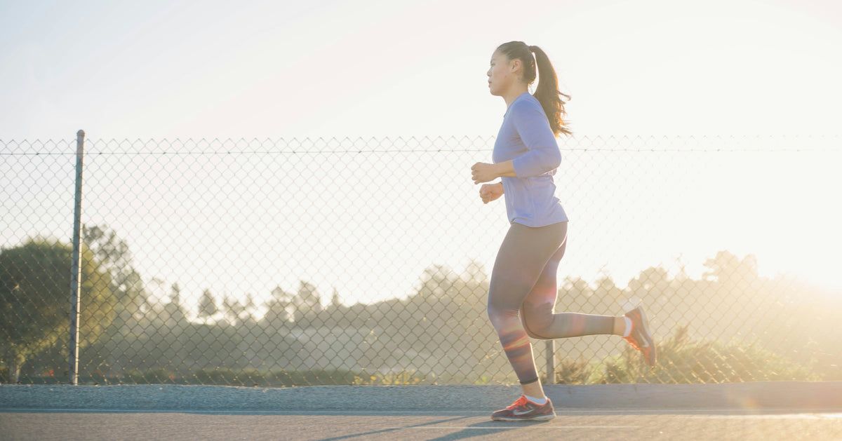 A woman in a blue top running beside a fence in warm sunlight.