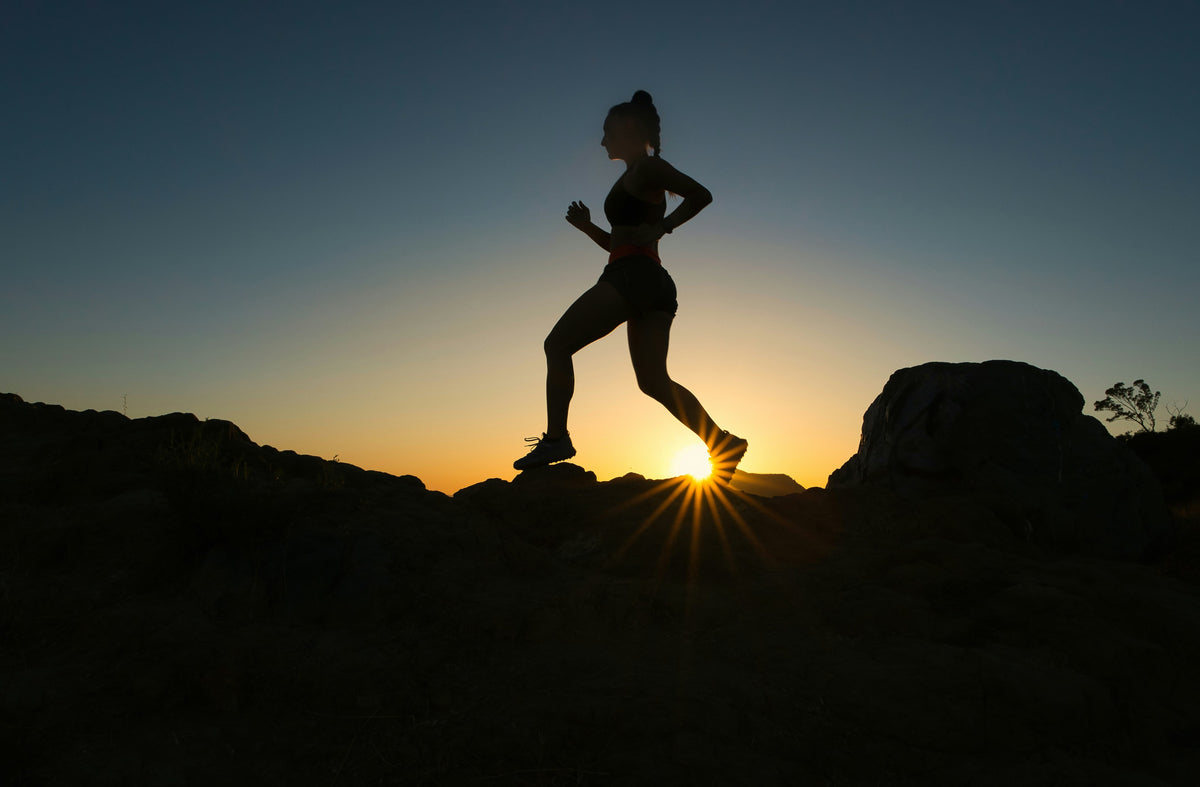 A runner silhouetted against a low sun on rocky ground.