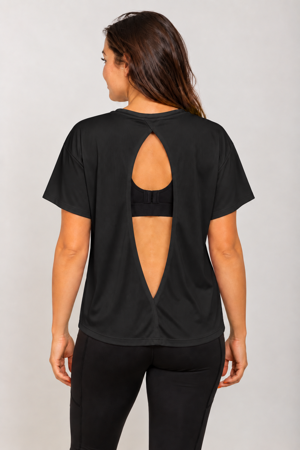 Black open-back Running Woman T-shirt on a brunette model viewed from behind with a black running bra visible through the open back