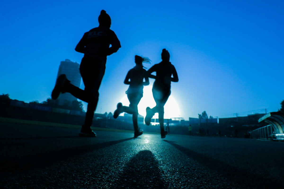 Three runners silhouetted on a track beneath a blue evening sky.